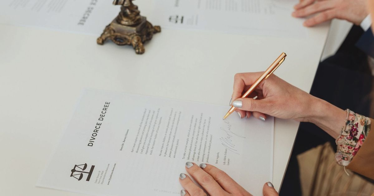 Close-up of hands signing a divorce decree document on a desk, showcasing legal process.