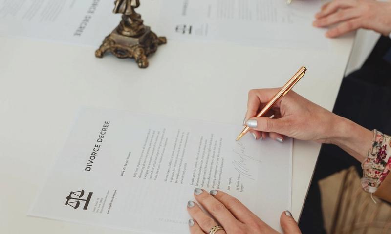 Close-up of hands signing a divorce decree document on a desk, showcasing legal process.