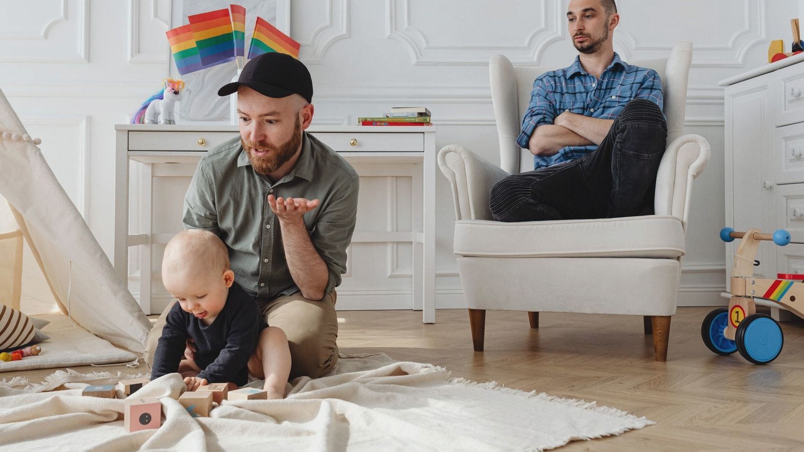 A same-sex couple with their child playing indoors, highlighting modern parenting.