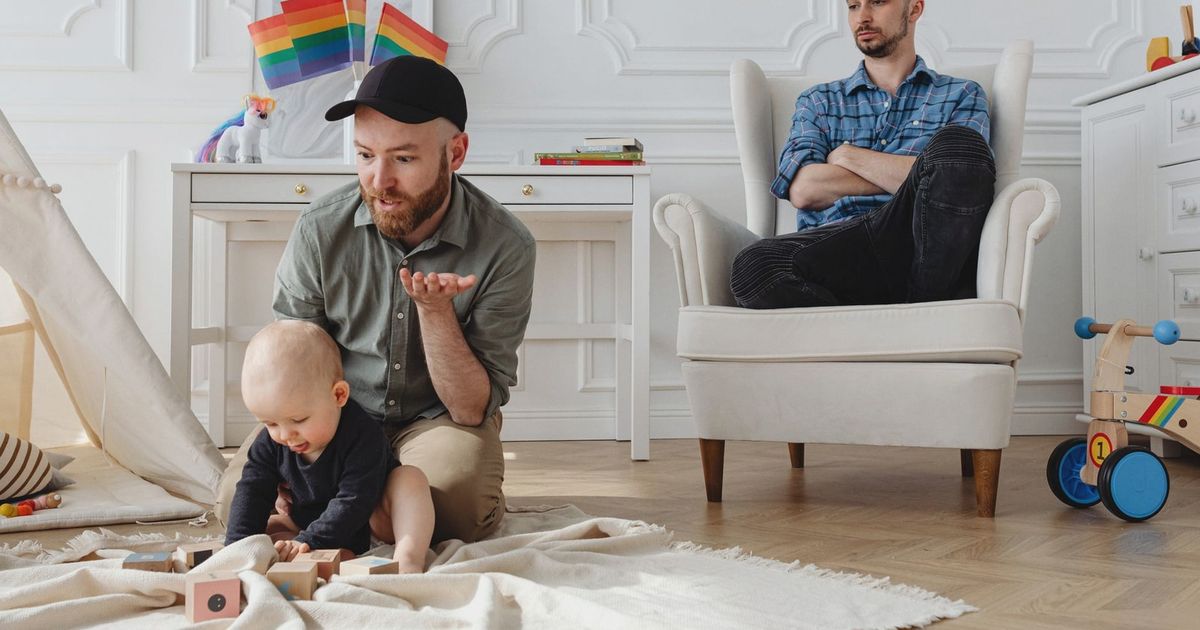 A same-sex couple with their child playing indoors, highlighting modern parenting.