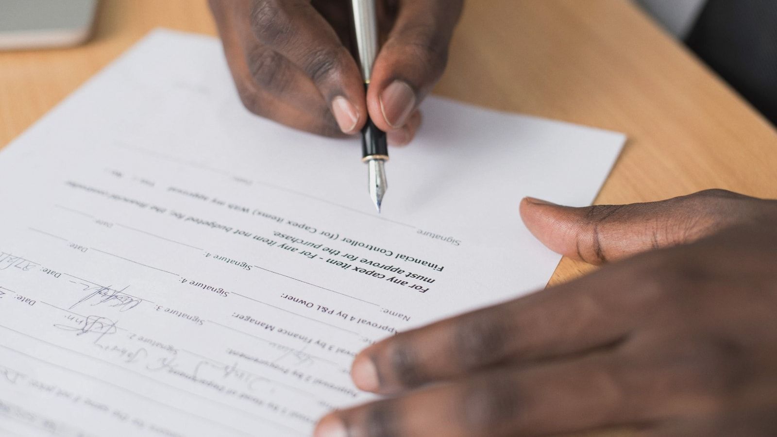 Close-up of a man's hands signing a formal document indoors.