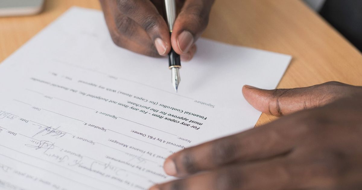 Close-up of a man's hands signing a formal document indoors.