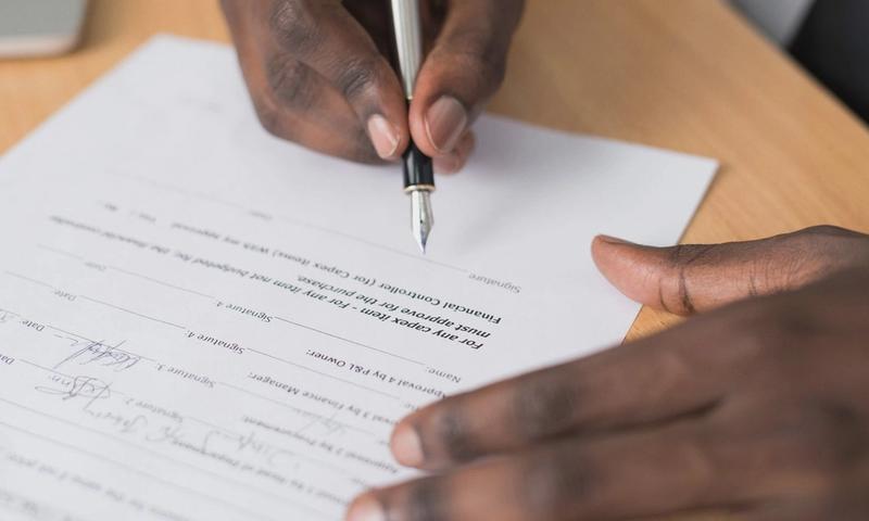 Close-up of a man's hands signing a formal document indoors.