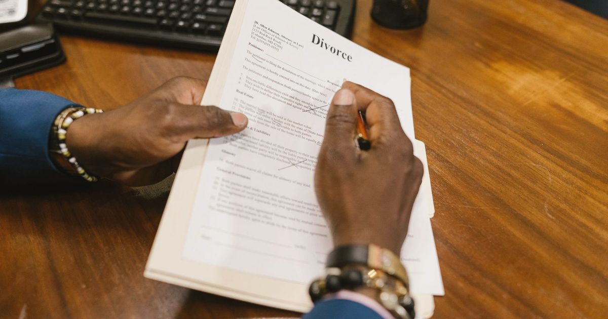 A person signs official divorce documents at an office desk.