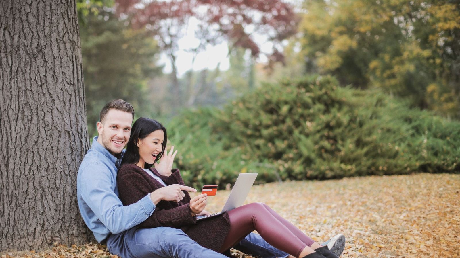A joyful couple using a laptop and credit card outdoors during fall.