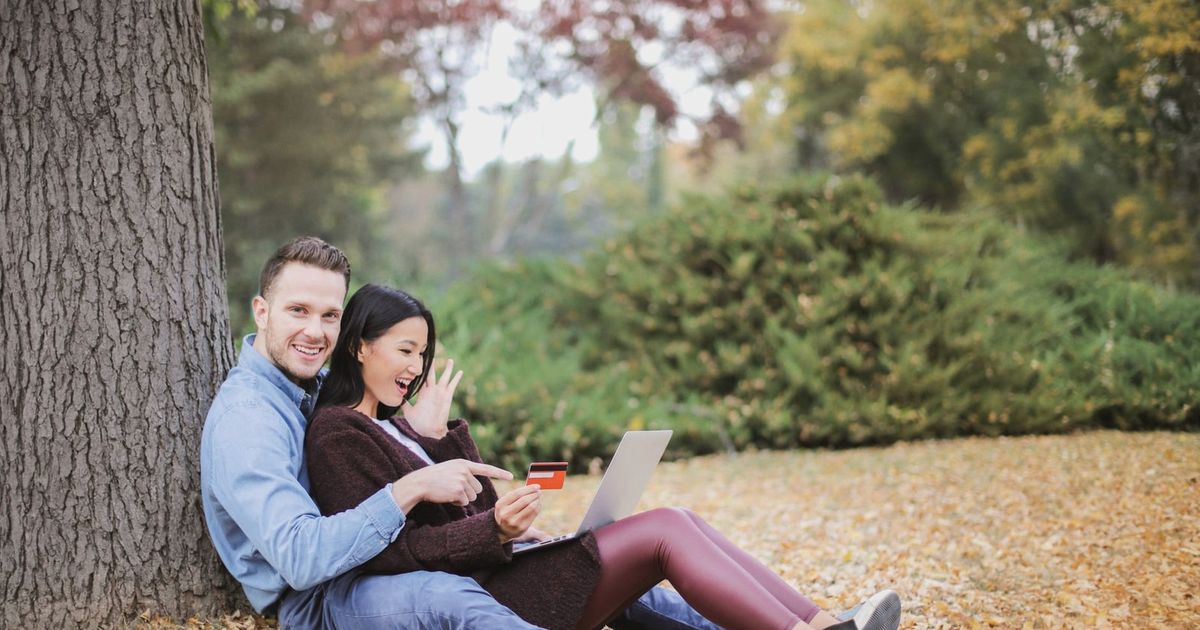 A joyful couple using a laptop and credit card outdoors during fall.