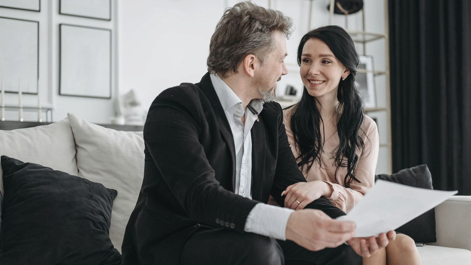 Couple smiling while sitting on a couch reviewing documents indoors.