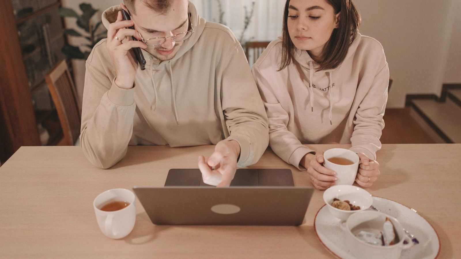 A couple enjoying coffee and online shopping together at home, using a laptop and smartphone.