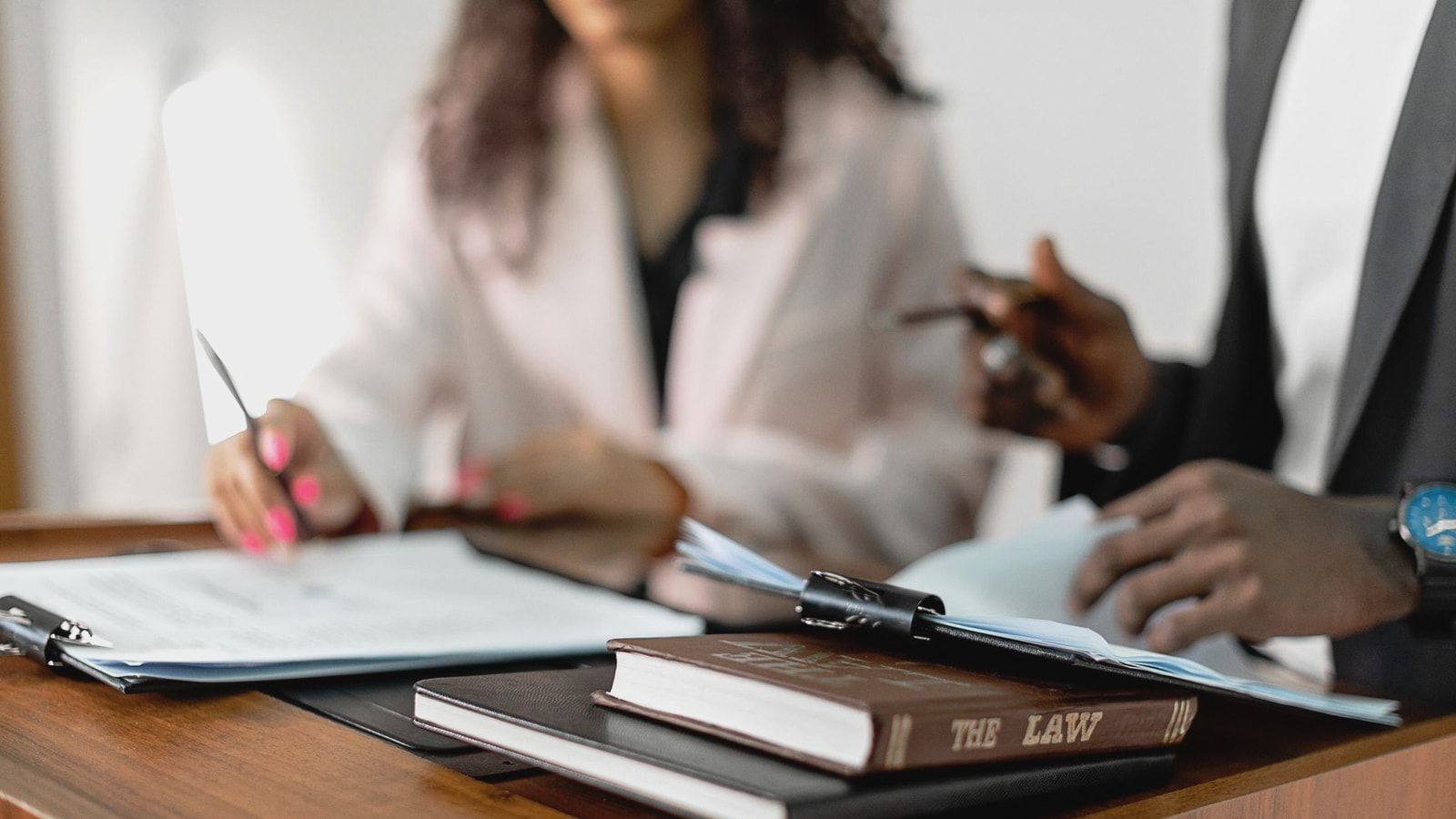 Two lawyers reviewing documents with law books on a desk. Professional legal environment.