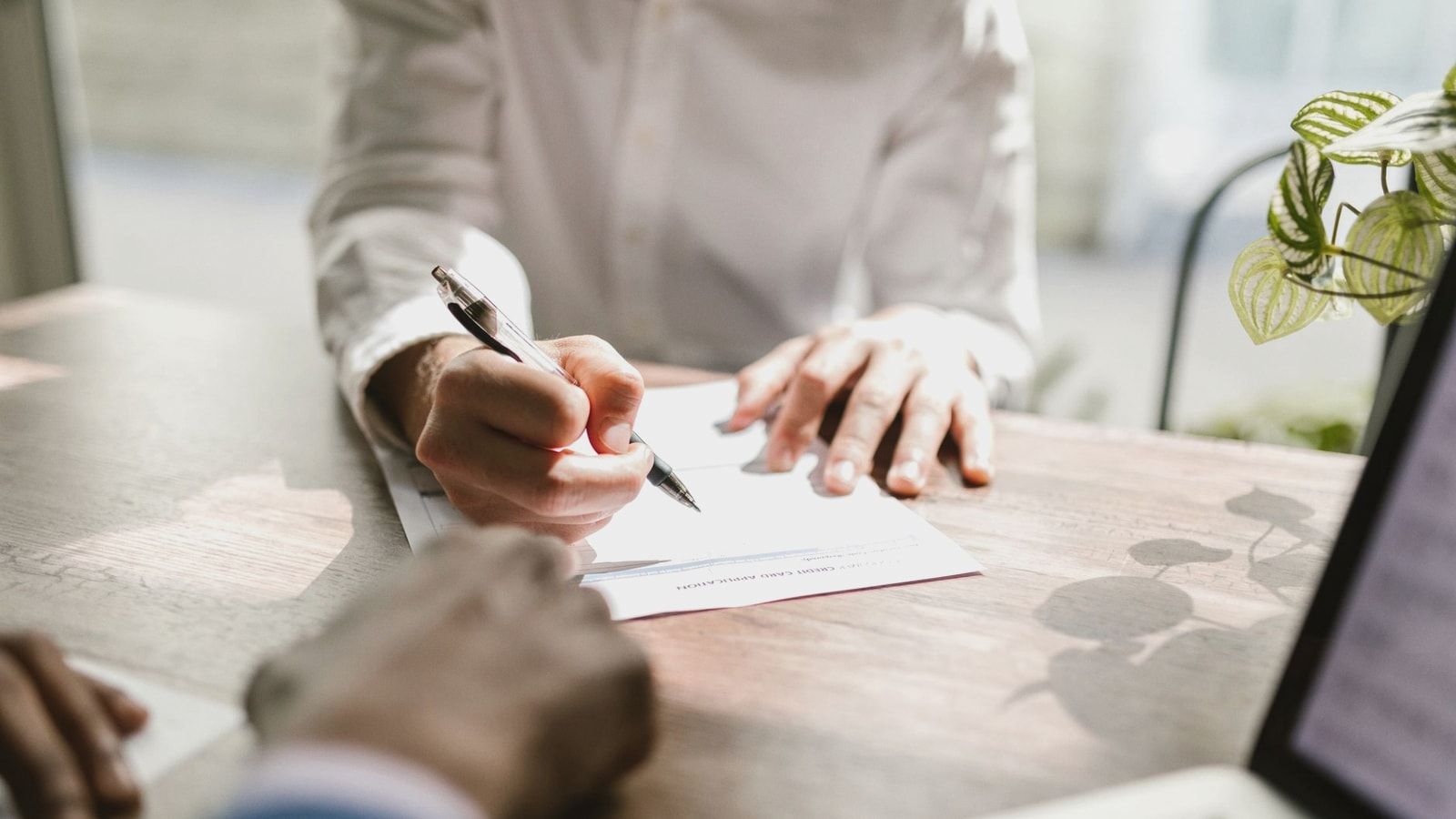 Close-up of people signing a document at a desk, highlighting professional business interaction.