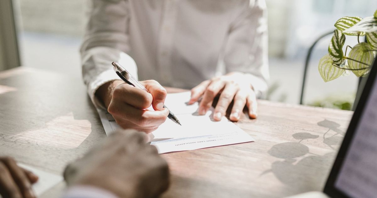 Close-up of people signing a document at a desk, highlighting professional business interaction.