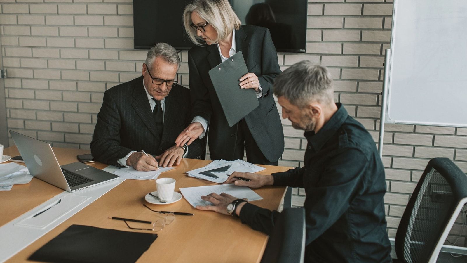 Three mature professionals in a business meeting discussing and signing documents in an office setting.