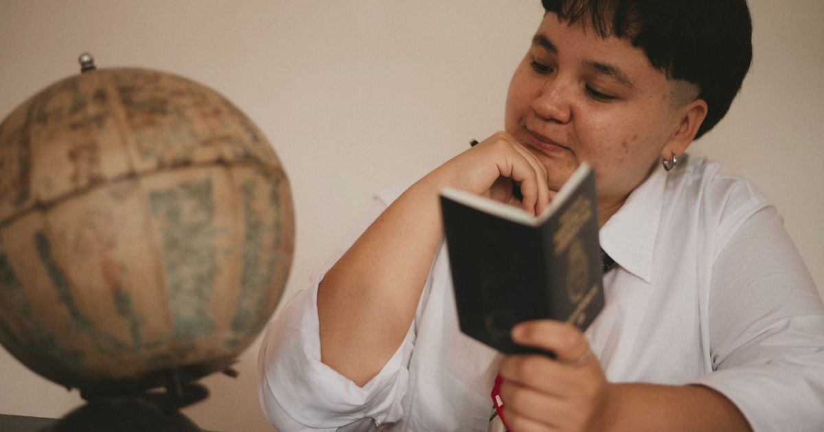 A pensive young adult reading a passport next to a vintage globe, symbolizing travel dreams.