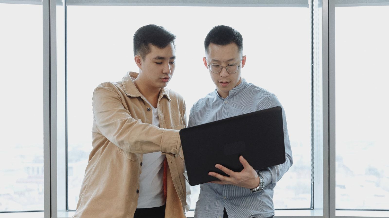 Two young professionals in an office setting, collaborating on a project using a laptop.