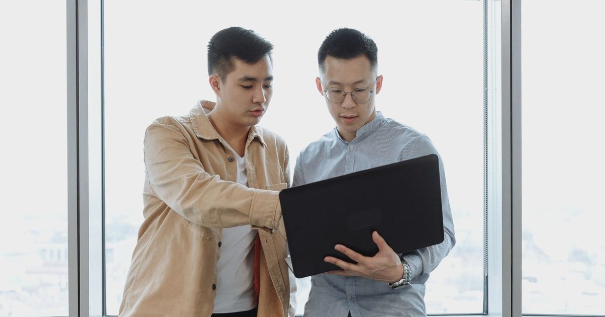 Two young professionals in an office setting, collaborating on a project using a laptop.