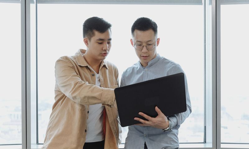 Two young professionals in an office setting, collaborating on a project using a laptop.