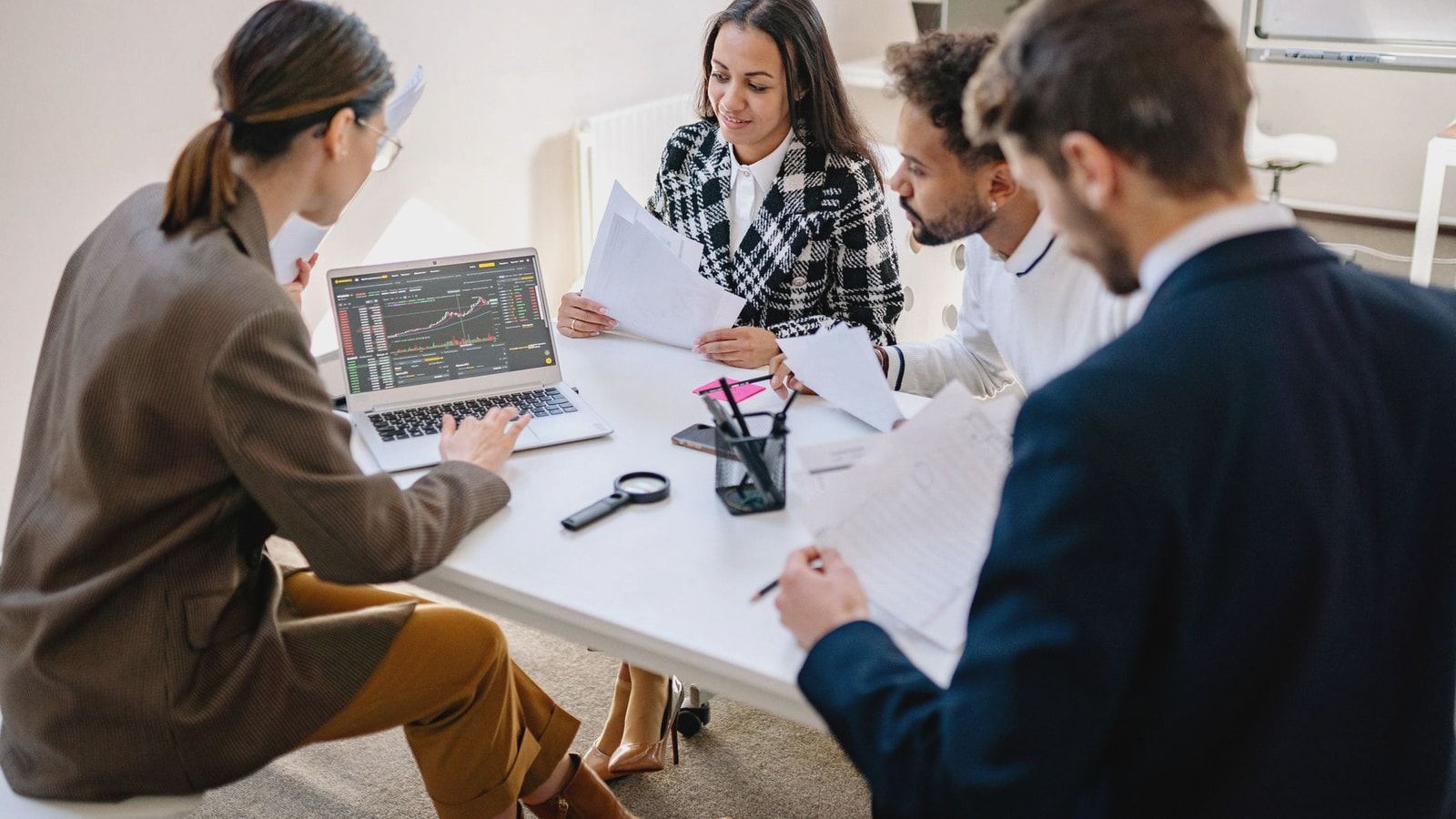 A team of diverse professionals collaborating and analyzing data on a laptop in an office meeting.