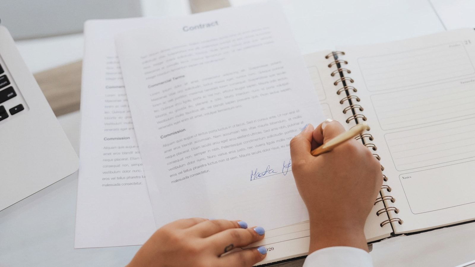 Close-up of hands signing a contract on a desk with office supplies, symbolizing legal agreements.