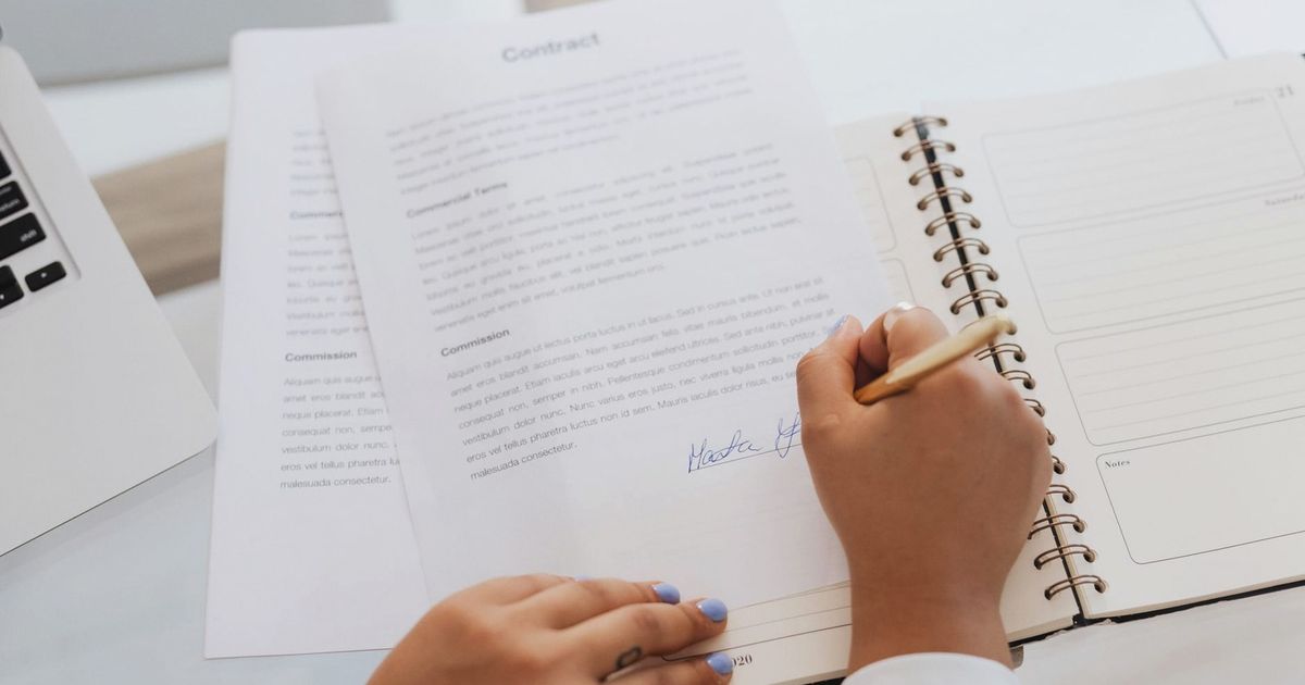 Close-up of hands signing a contract on a desk with office supplies, symbolizing legal agreements.