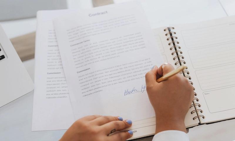 Close-up of hands signing a contract on a desk with office supplies, symbolizing legal agreements.