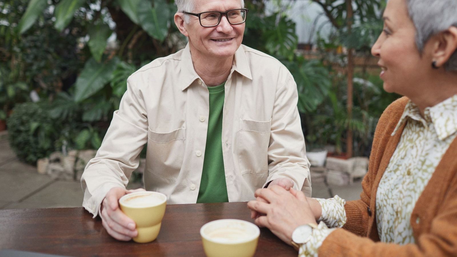 Happy senior couple sharing coffee and conversation in a lush garden setting.