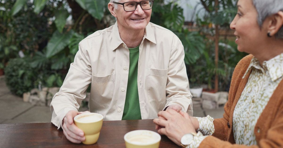 Happy senior couple sharing coffee and conversation in a lush garden setting.