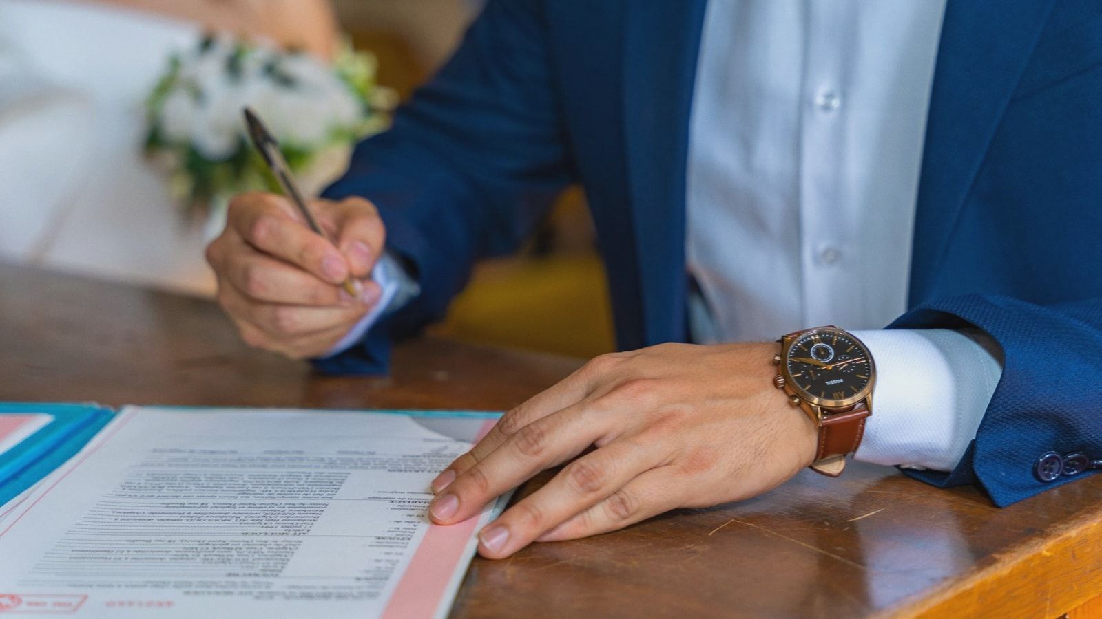 Close-up of groom signing wedding documents with bride nearby.