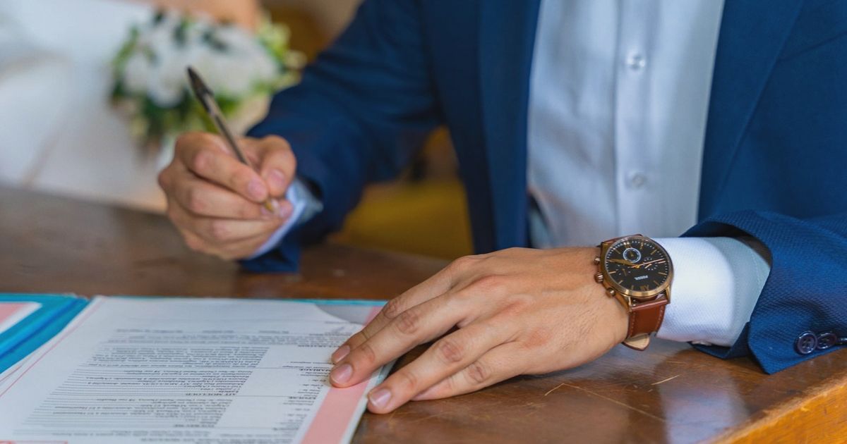 Close-up of groom signing wedding documents with bride nearby.