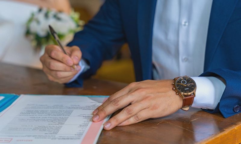 Close-up of groom signing wedding documents with bride nearby.