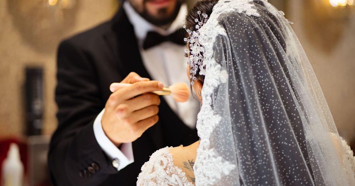 A bride receives makeup touch-up by groom before her wedding ceremony.