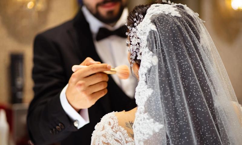 A bride receives makeup touch-up by groom before her wedding ceremony.