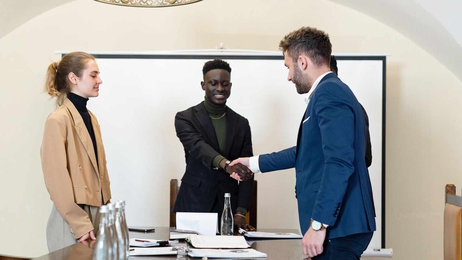 A diverse group of business professionals in a meeting room, shaking hands as a sign of agreement.