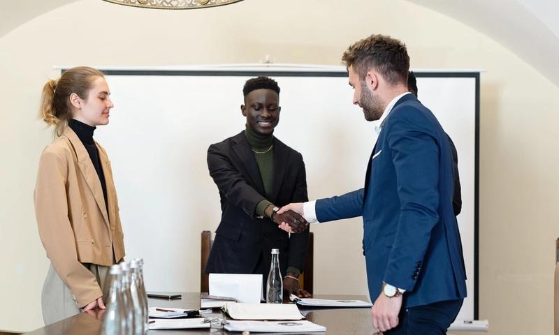 A diverse group of business professionals in a meeting room, shaking hands as a sign of agreement.