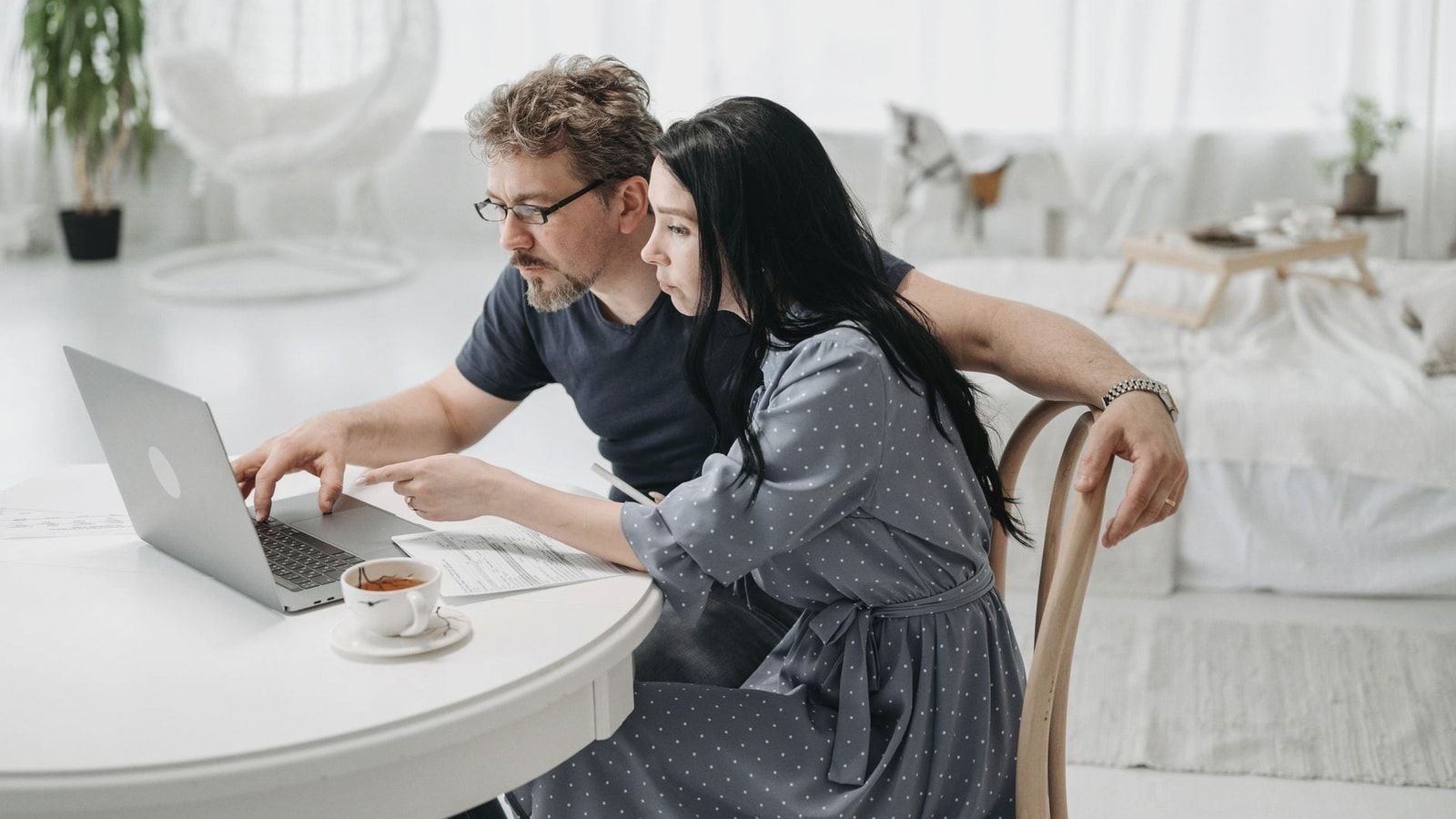 A man and woman sitting indoors, collaborating on a laptop at a table with coffee.