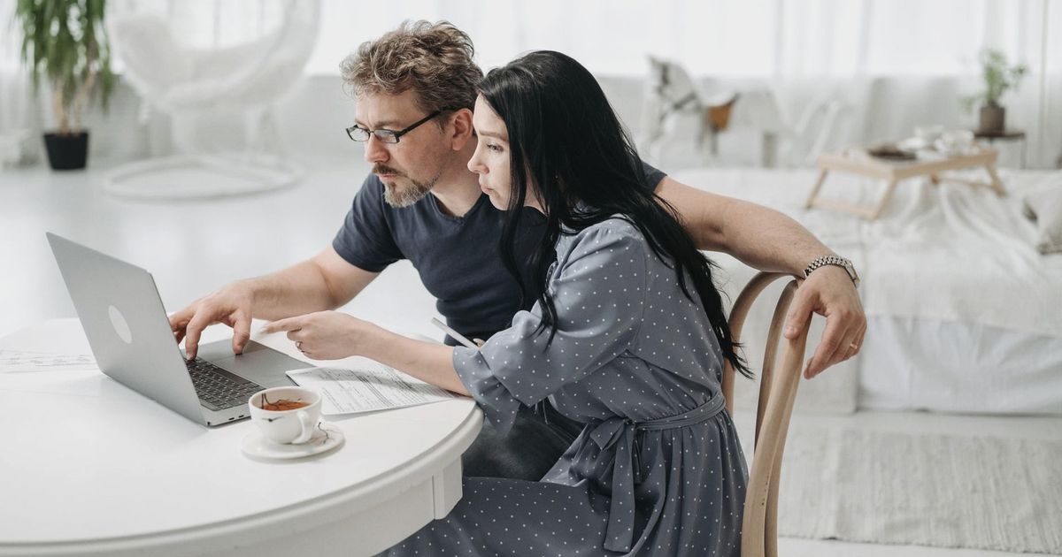 A man and woman sitting indoors, collaborating on a laptop at a table with coffee.