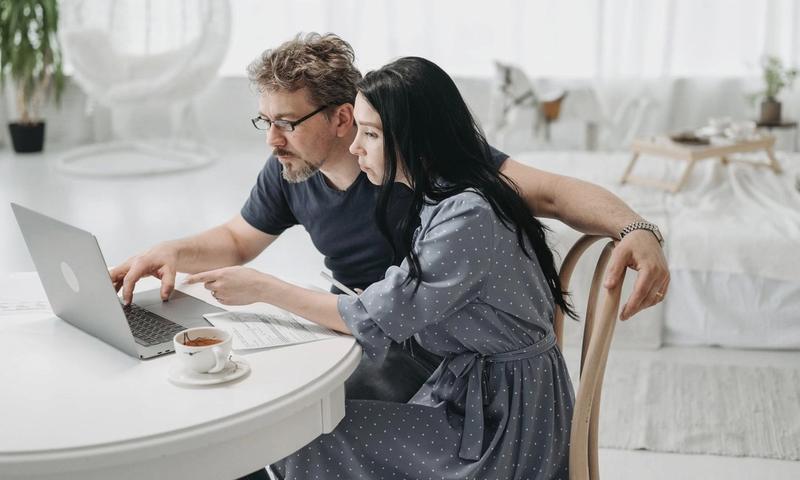 A man and woman sitting indoors, collaborating on a laptop at a table with coffee.