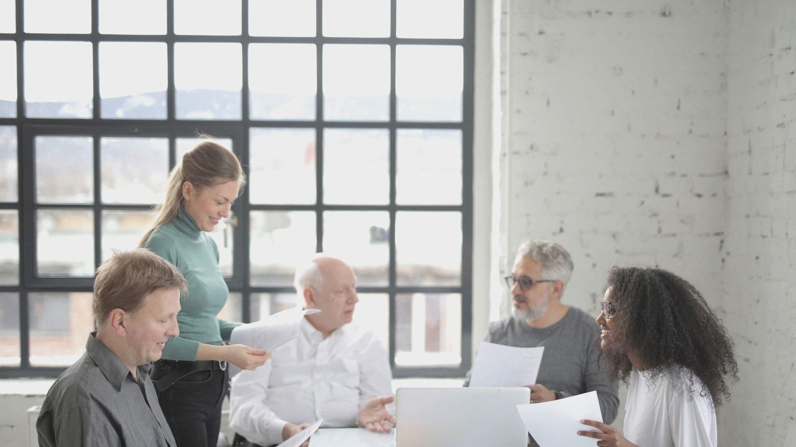 Group of diverse colleagues in casual wear brainstorming together at table with laptop while working with papers in creative office workspace