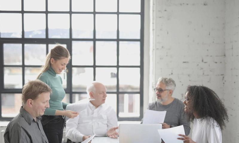 Group of diverse colleagues in casual wear brainstorming together at table with laptop while working with papers in creative office workspace