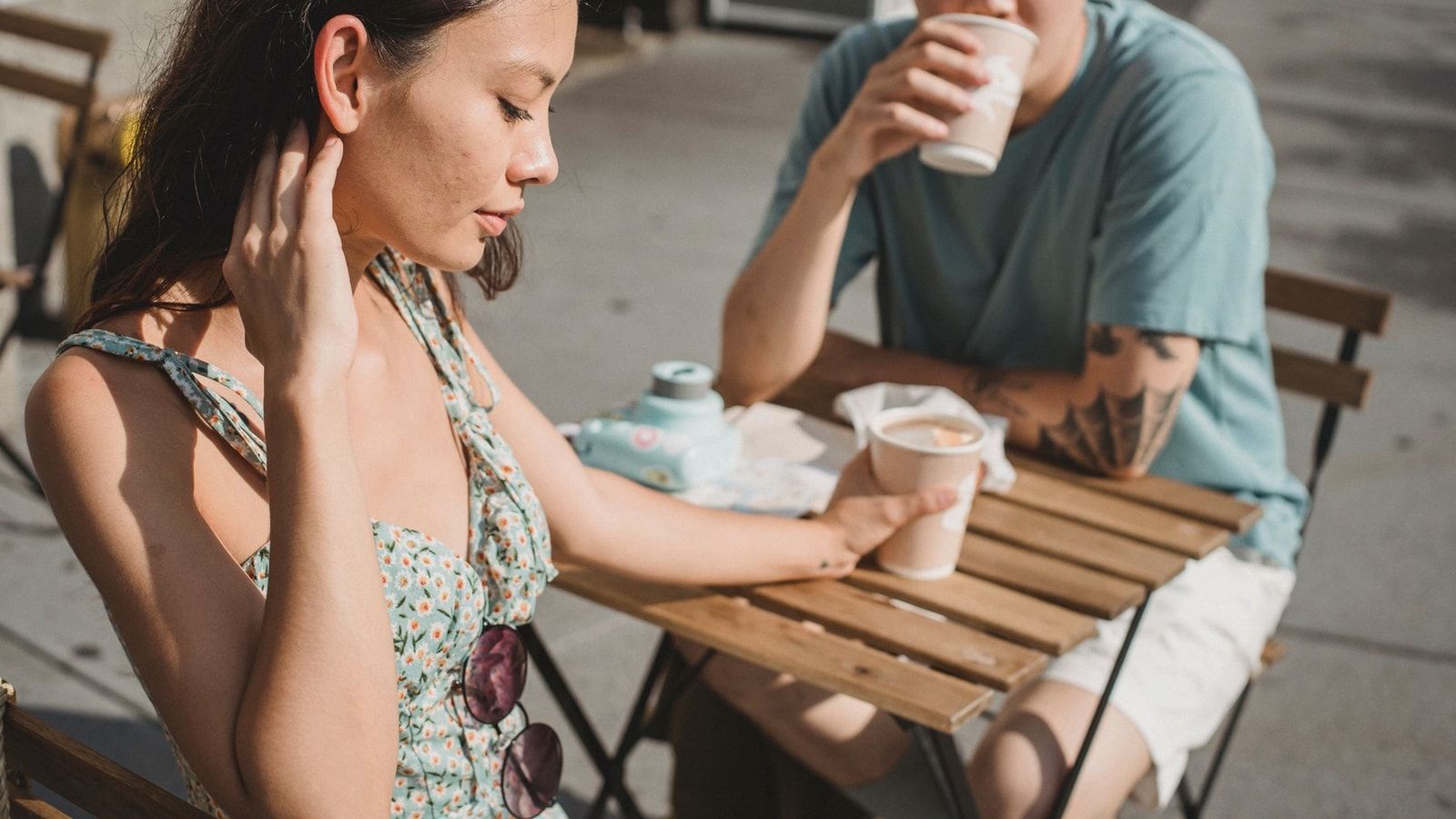 Young tender dreamy girlfriend and Asian pensive boyfriend with cup of hot coffee on sunny street