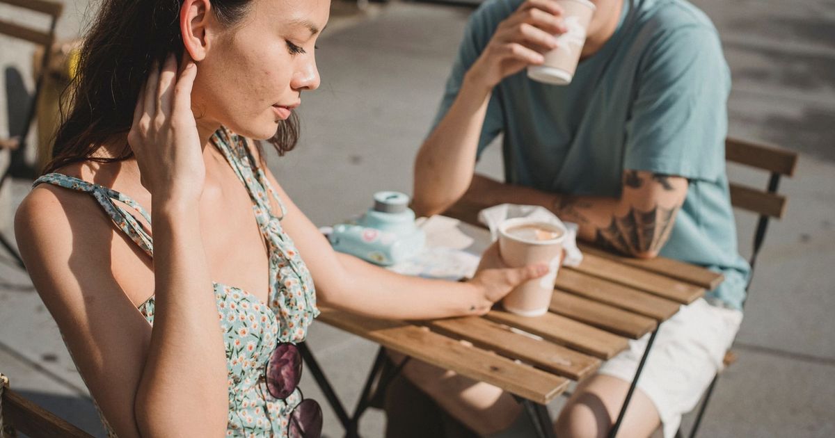 Young tender dreamy girlfriend and Asian pensive boyfriend with cup of hot coffee on sunny street