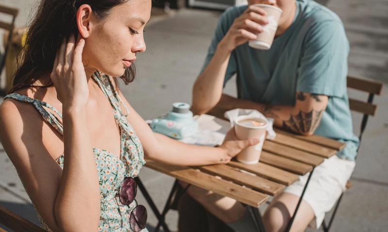 Young tender dreamy girlfriend and Asian pensive boyfriend with cup of hot coffee on sunny street