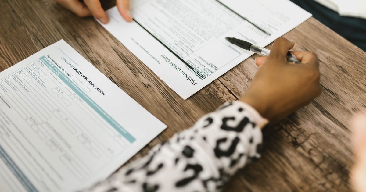 Close-up of two people reviewing and filling out a credit card application on a wooden table.