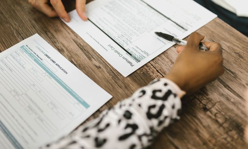 Close-up of two people reviewing and filling out a credit card application on a wooden table.