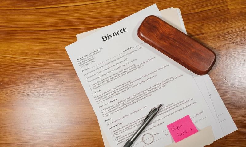Flat lay of divorce papers with a pen and ring on a wooden table for legal themes.