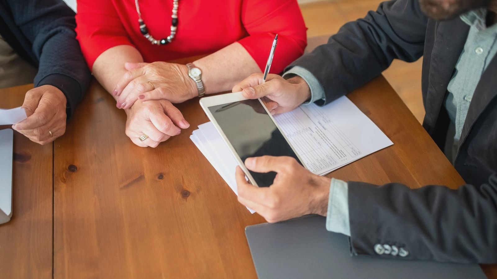 Business meeting at a wooden table with consultant reviewing documents and using a digital tablet.