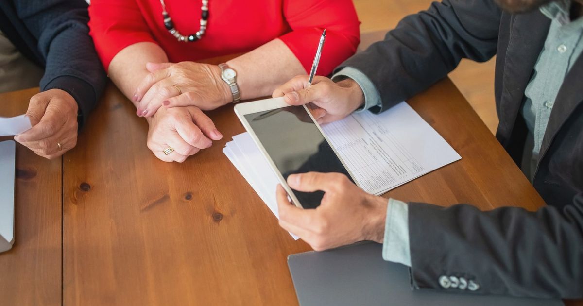 Business meeting at a wooden table with consultant reviewing documents and using a digital tablet.