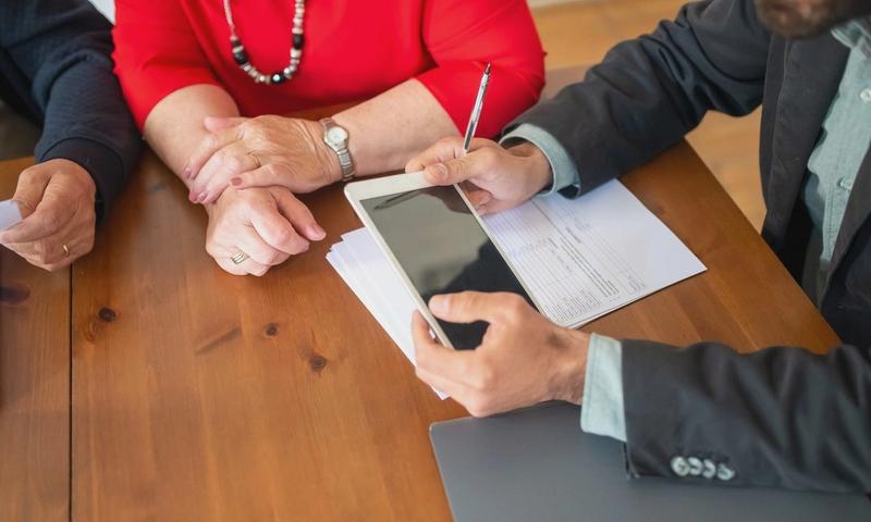 Business meeting at a wooden table with consultant reviewing documents and using a digital tablet.
