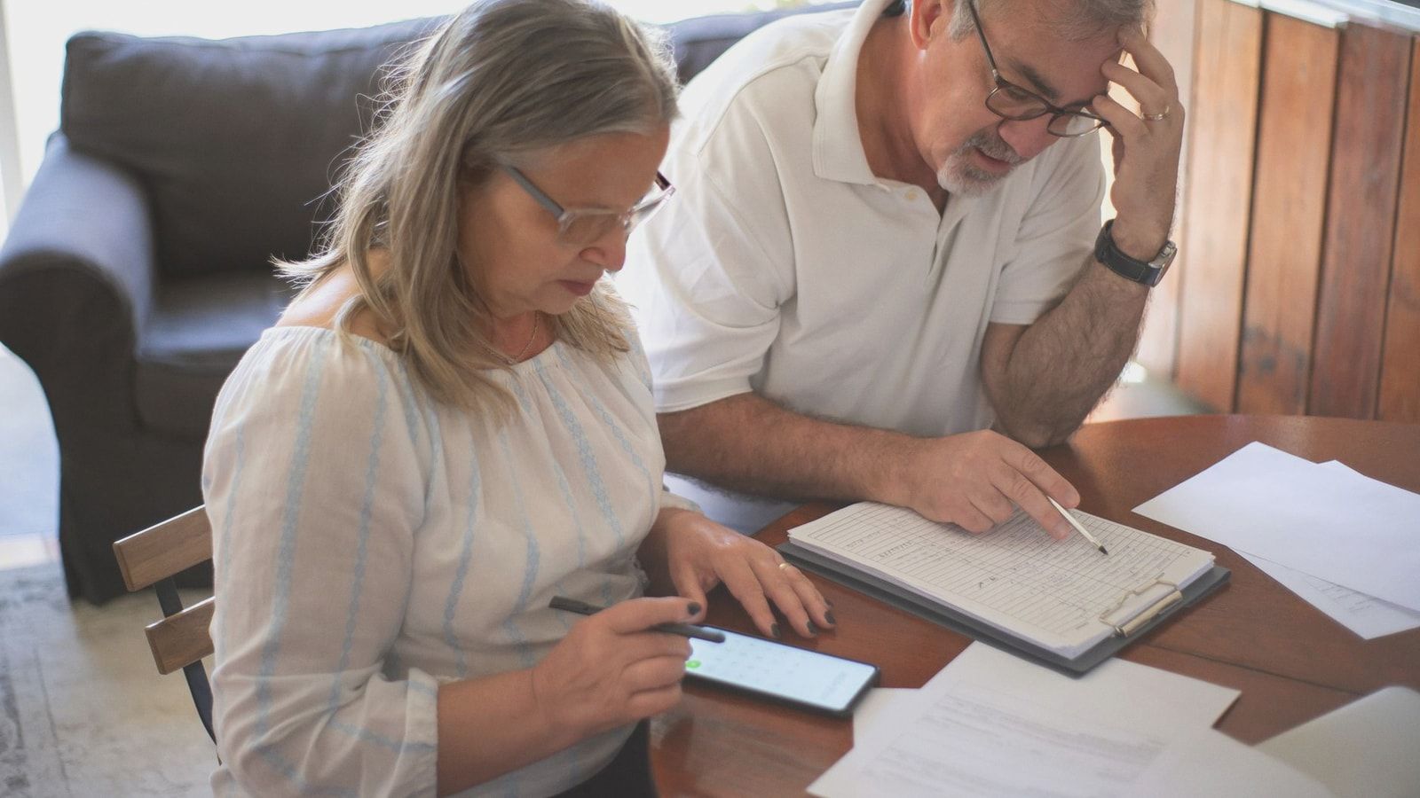 Elderly couple reviewing bills and documents at home, focusing on finances and technology.