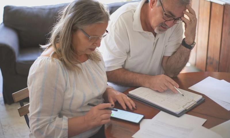 Elderly couple reviewing bills and documents at home, focusing on finances and technology.