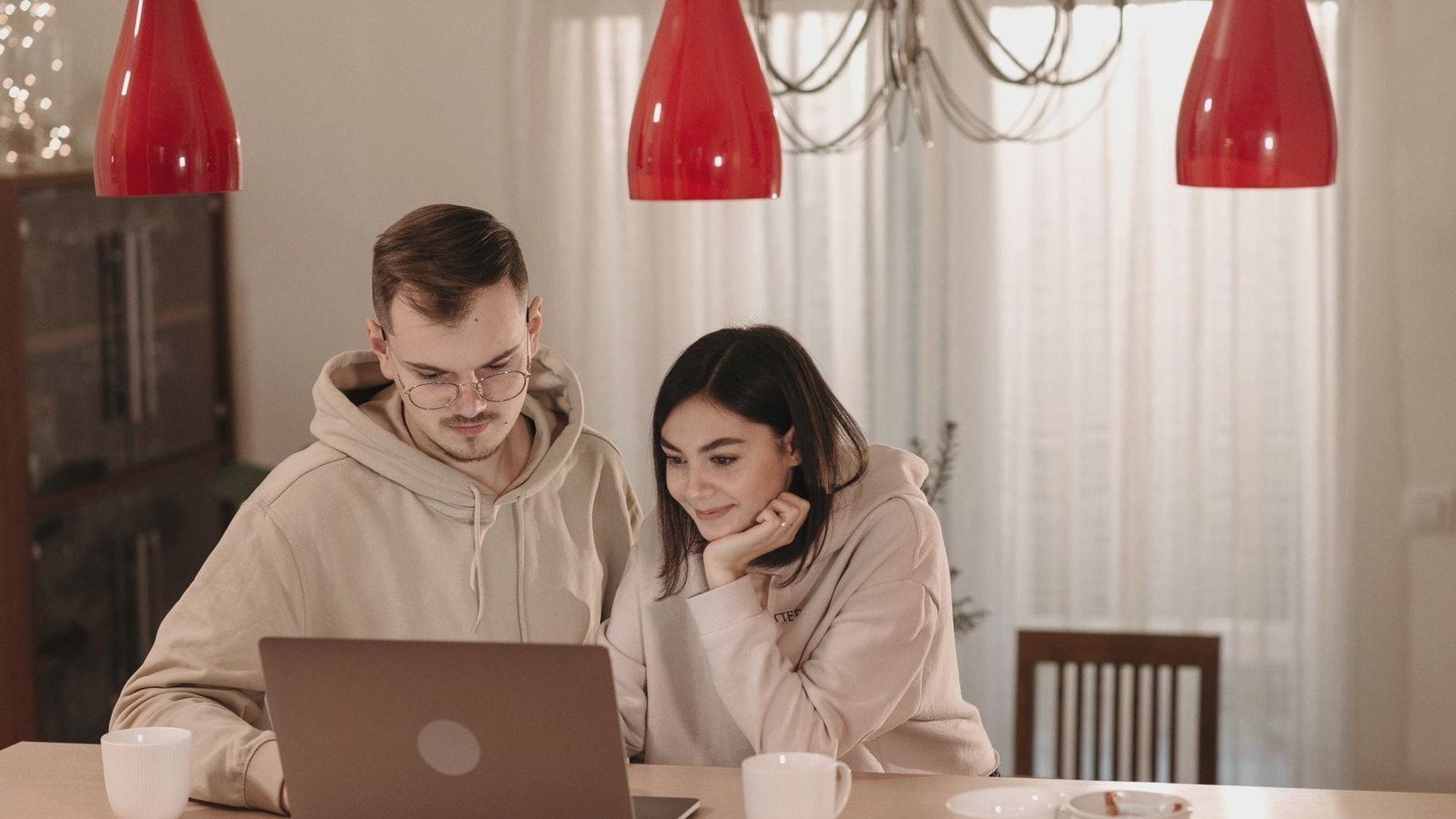 A couple in casual hoodies using a laptop at home, smiling and relaxed.